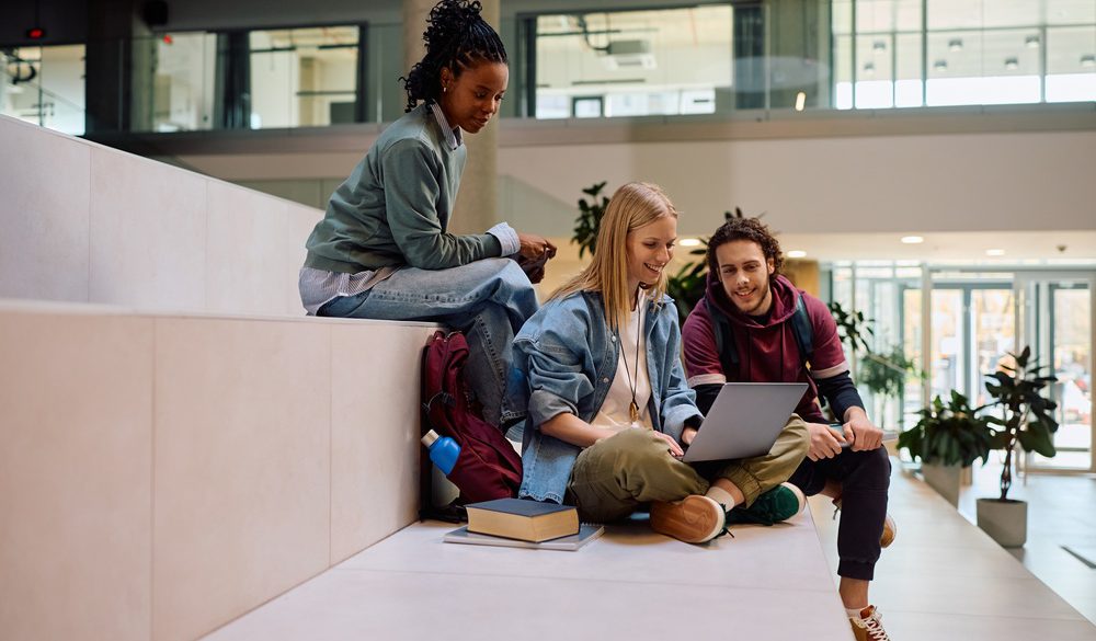 Grupa studentów uczy się wspólnie, siedząc na trawie z laptopami i notatkami