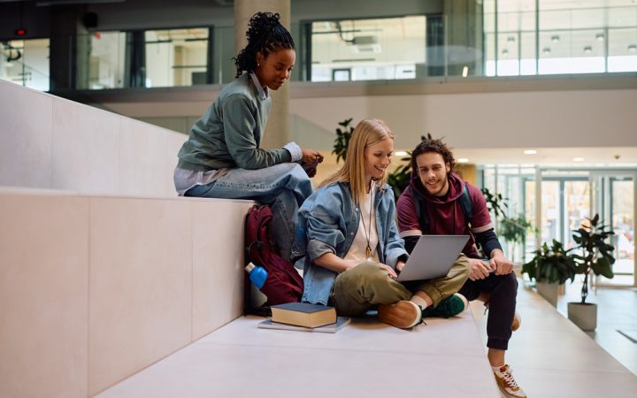 Grupa studentów uczy się wspólnie, siedząc na trawie z laptopami i notatkami